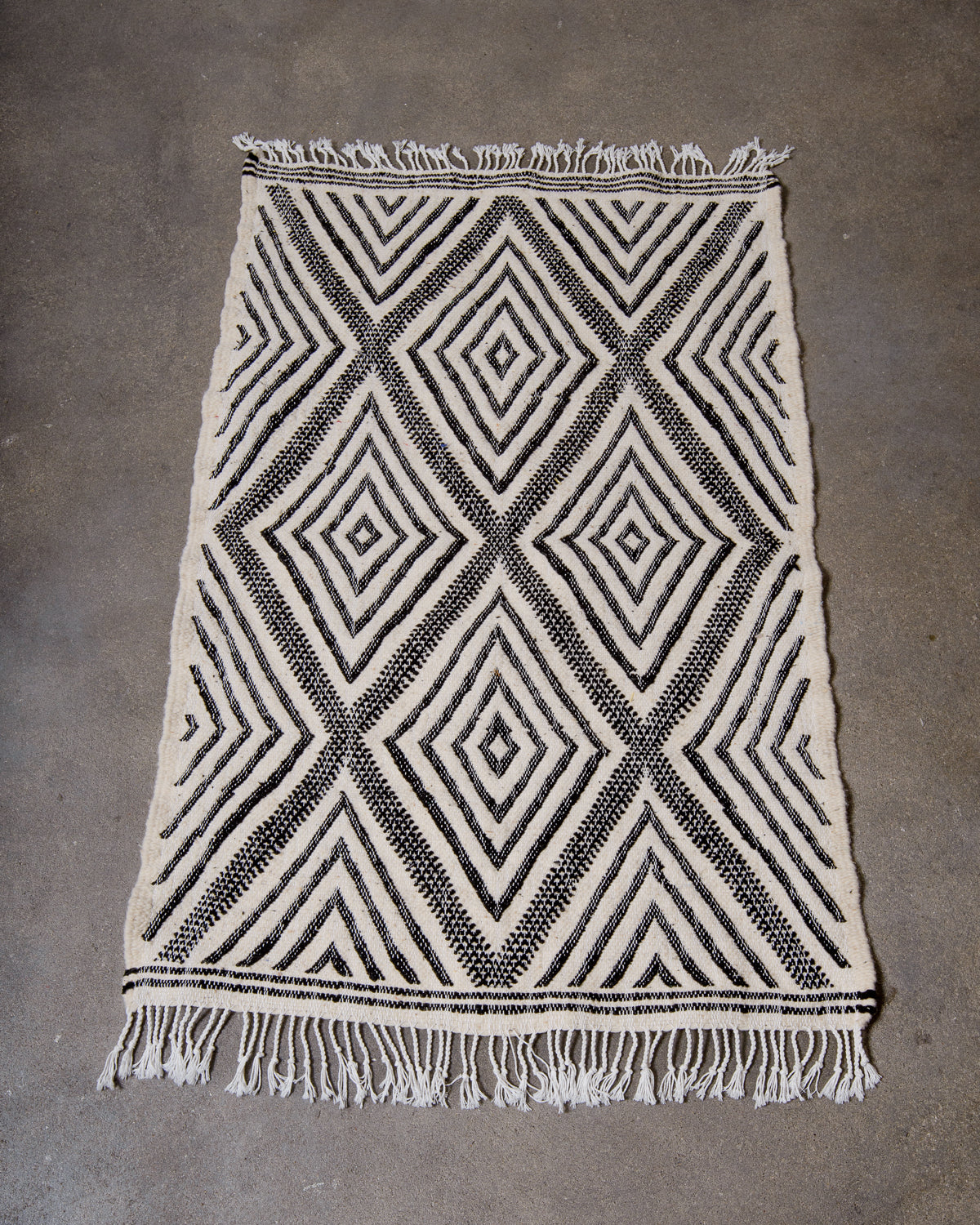 Small Kelim Rug in black and cream laying on concrete studio floor.
